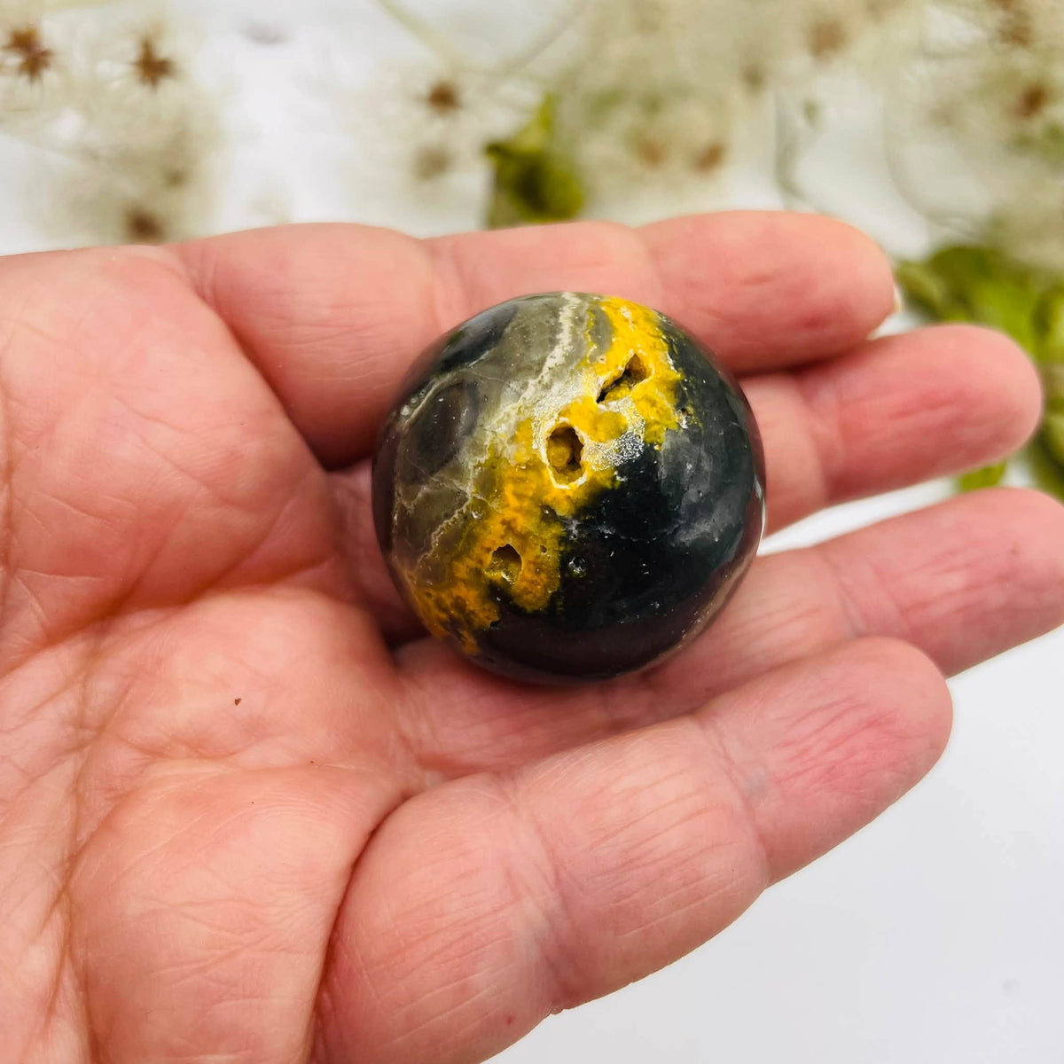 Bumblebee-Jaspis Kugel von oben in einer Hand, mit kontrastreicher gelb-dunkelgrauer Bänderung – handverlesen von WUNDERSTEIN
