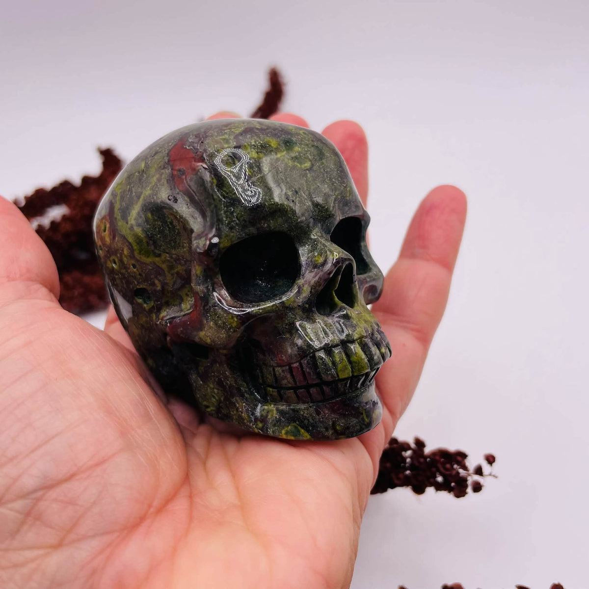 Nahaufnahme des Totenkopfs aus Drachenblut-Jaspis: dunkelgrüne Musterung mit roten Einschlüssen und glänzend polierter Oberfläche

