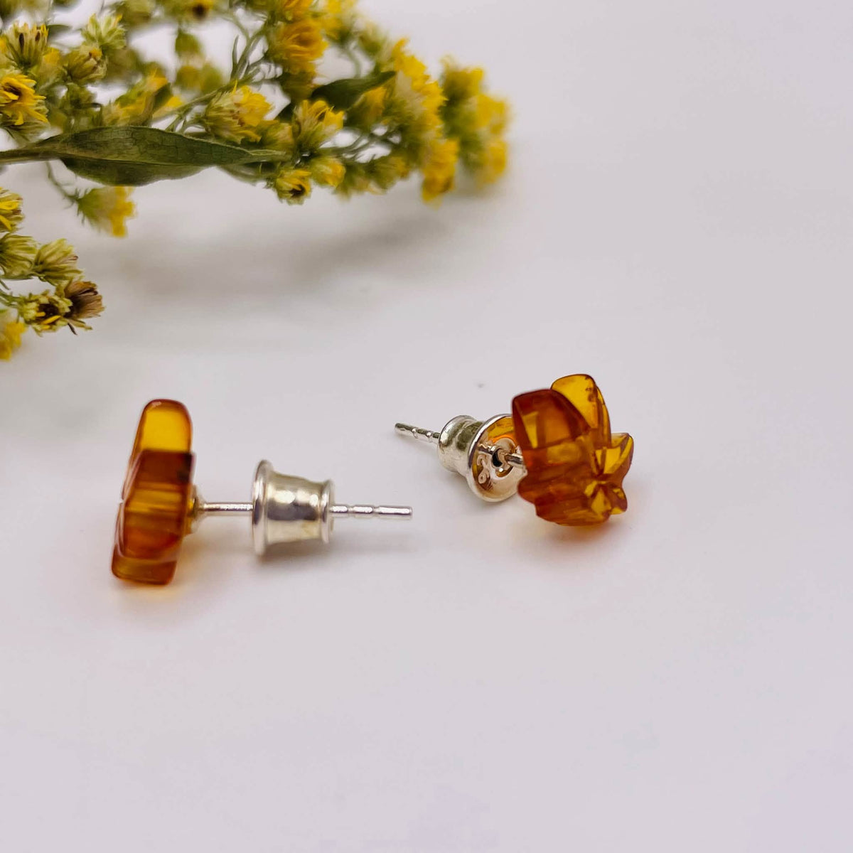 Nahaufnahme der Bernstein-Ohrstecker in Hanfblatt-Form mit warmen goldenen Farbnuancen und natürlichen Kristalldetails
