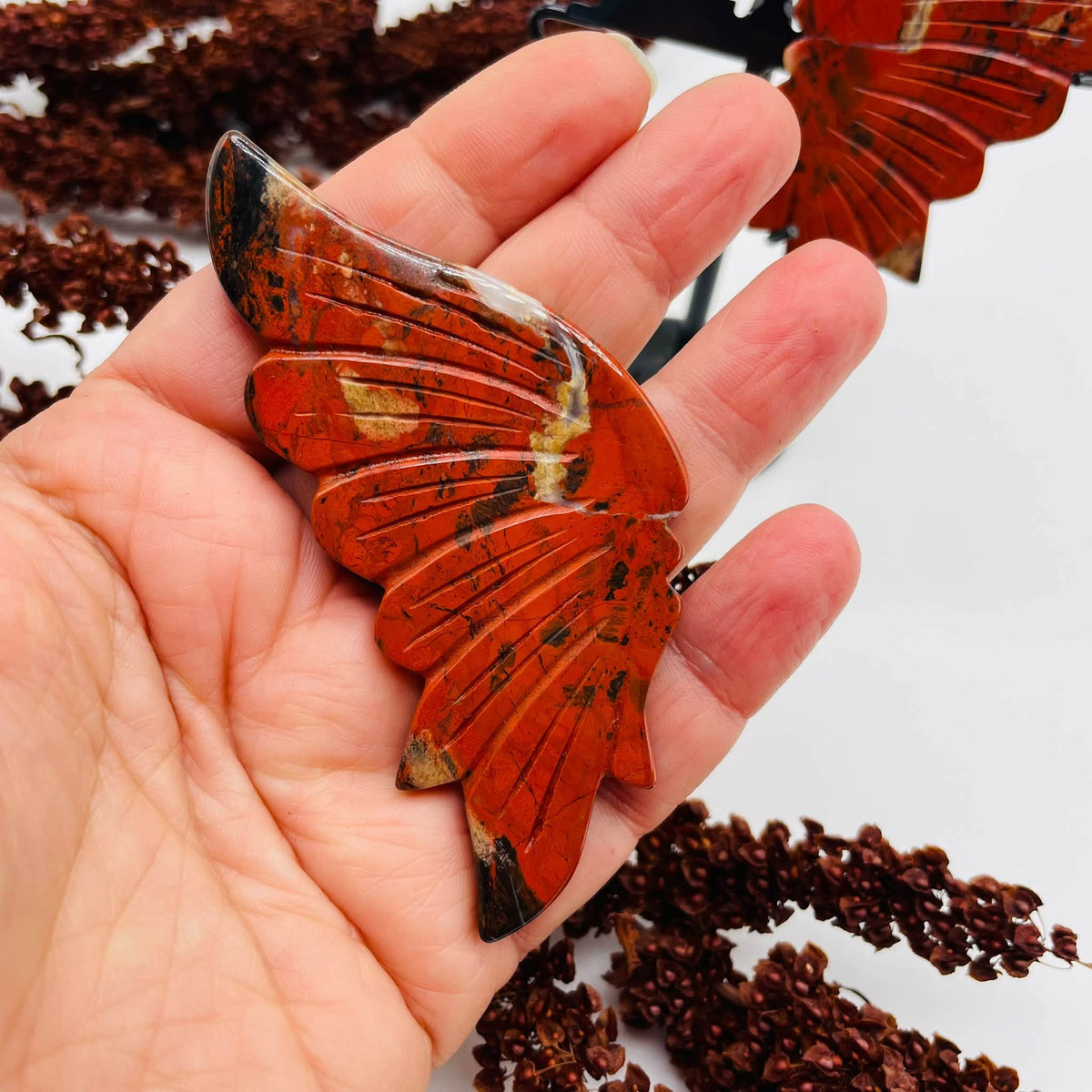 Nahaufnahme der aus rotem Jaspis gearbeiteten Schmetterlingsflügel mit tiefroter, schwarz-cremefleckter Struktur und feinen Flügeladern
