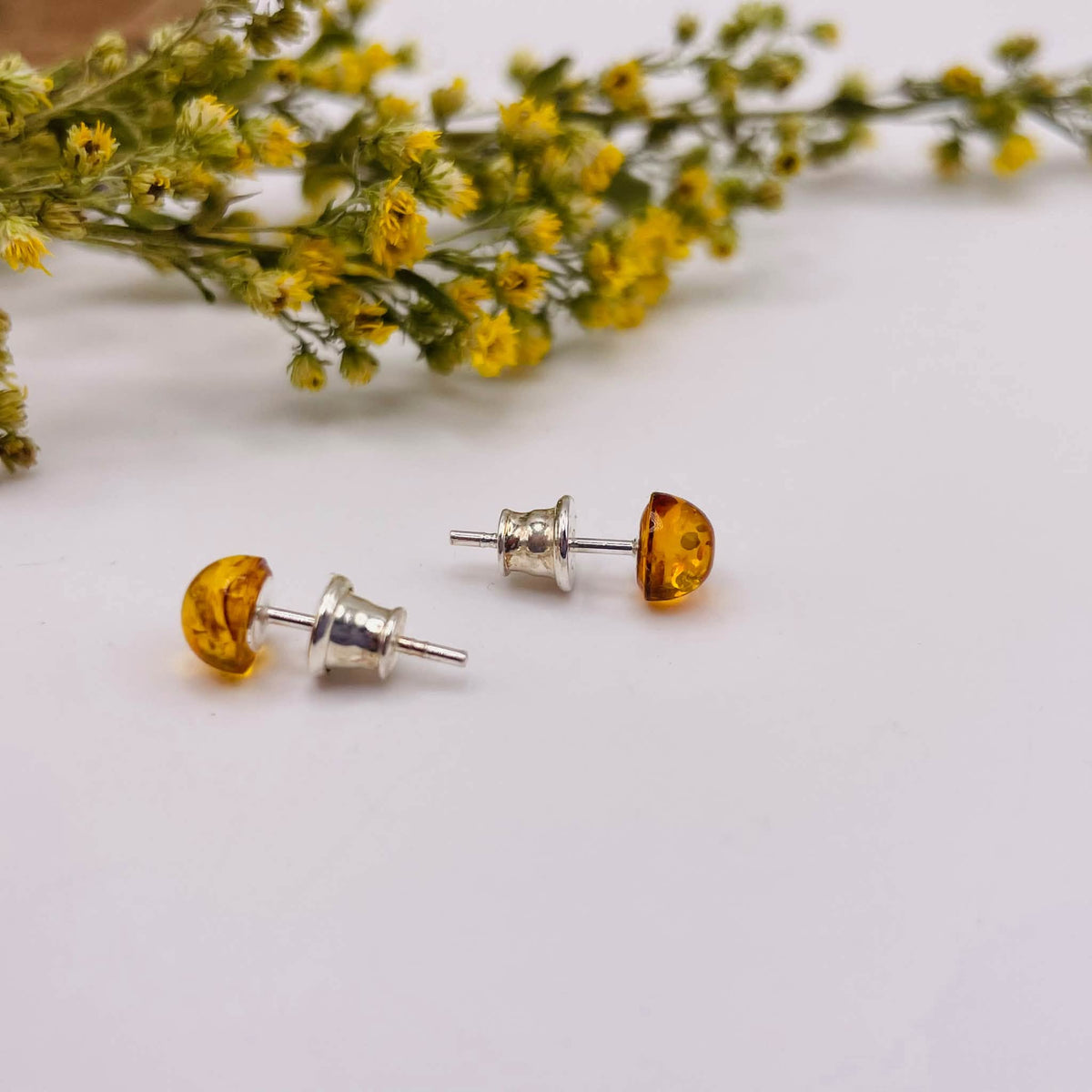 Nahaufnahme der runden Bernstein-Ohrstecker in Halbkugelform aus 925er Silber mit warmen natürlichen Strukturen und goldener Farbgebung

