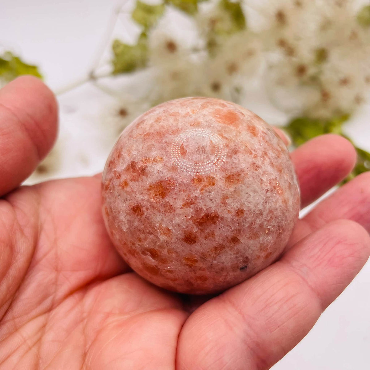 Sonnenstein Kugel von oben in einer Hand, mit pfirsichfarbener Zeichnung und glänzender Oberfläche – handverlesen von WUNDERSTEIN
